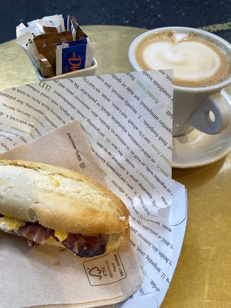 A cappuccino with latte art beside a breakfast baguette